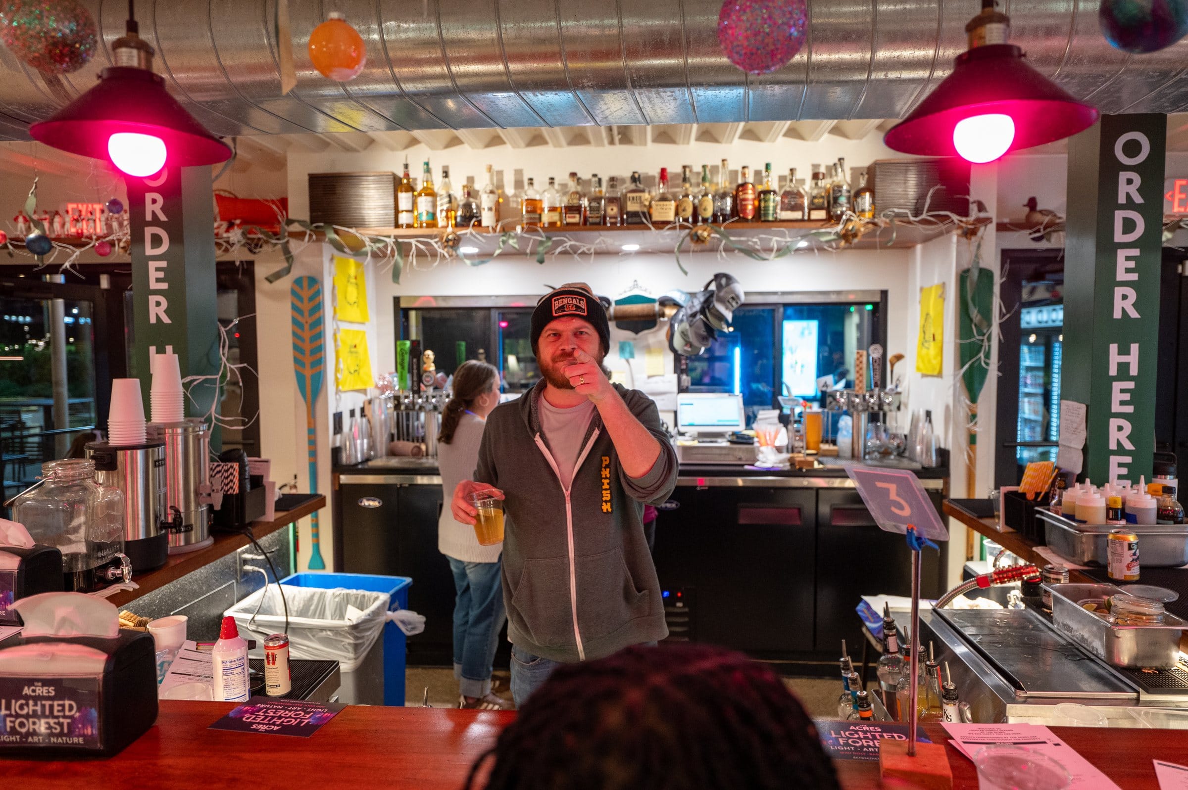 The Acres bar at night, with a bartender raising a glass under red pendant lights