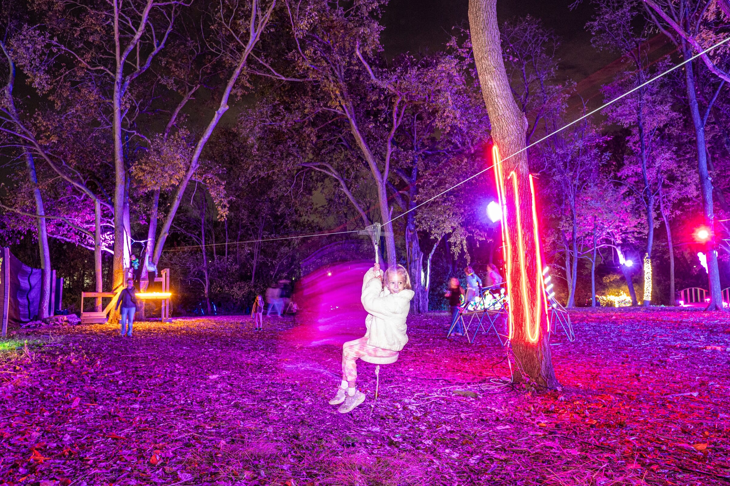 A child riding a zip line through trees lit purple and red