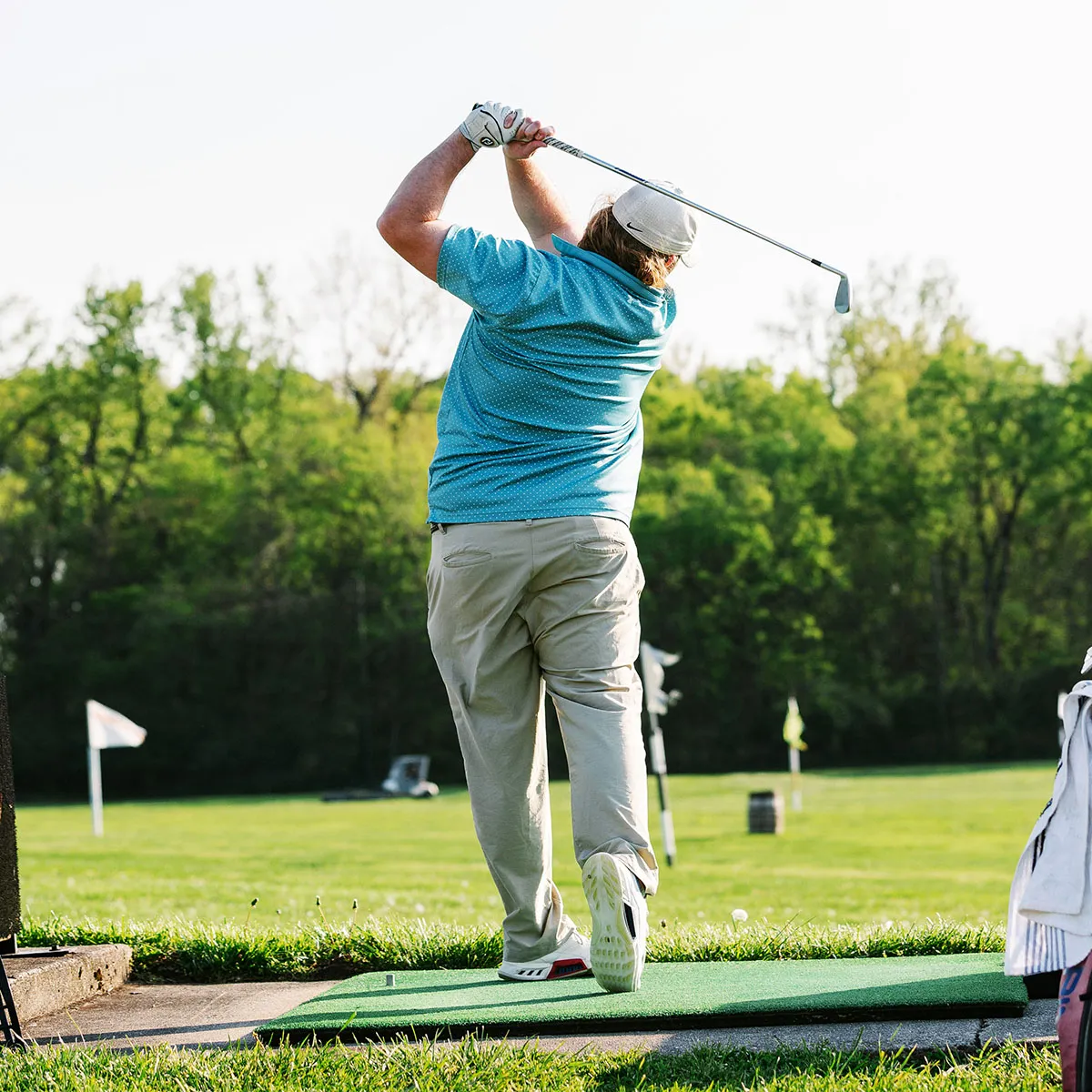 Golfer mid-swing at The Acres driving range with course flags beyond