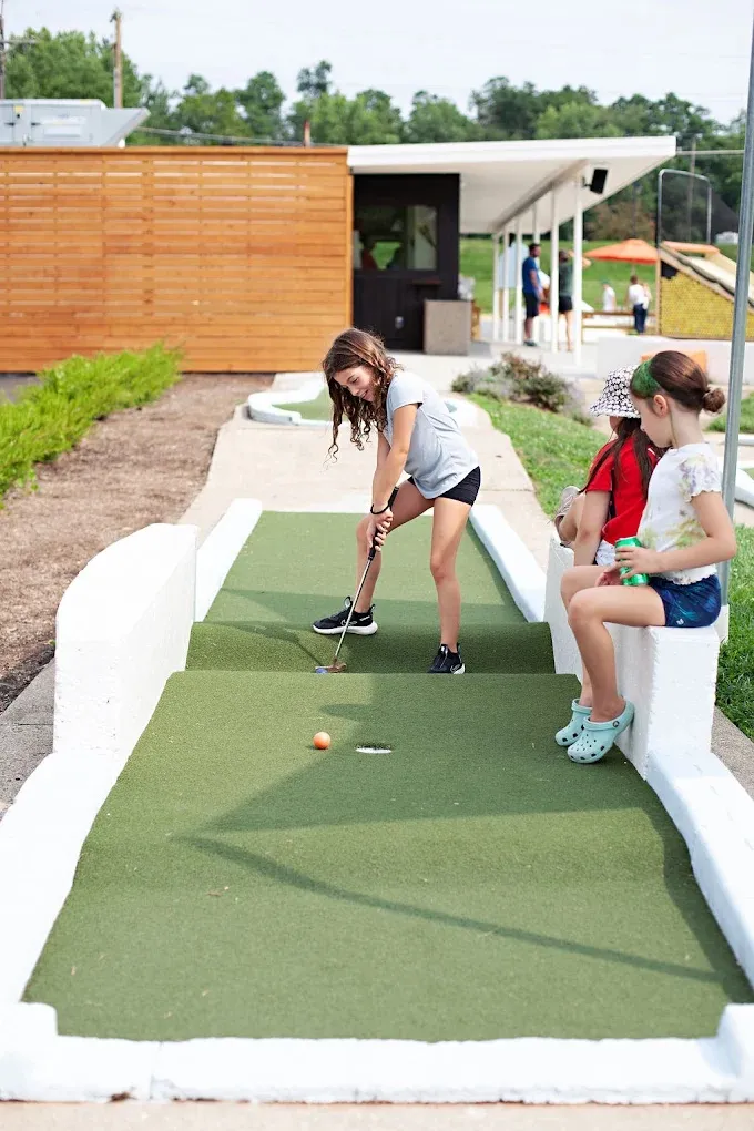 A young guest putting on a mini golf course at The Acres while a friend looks on