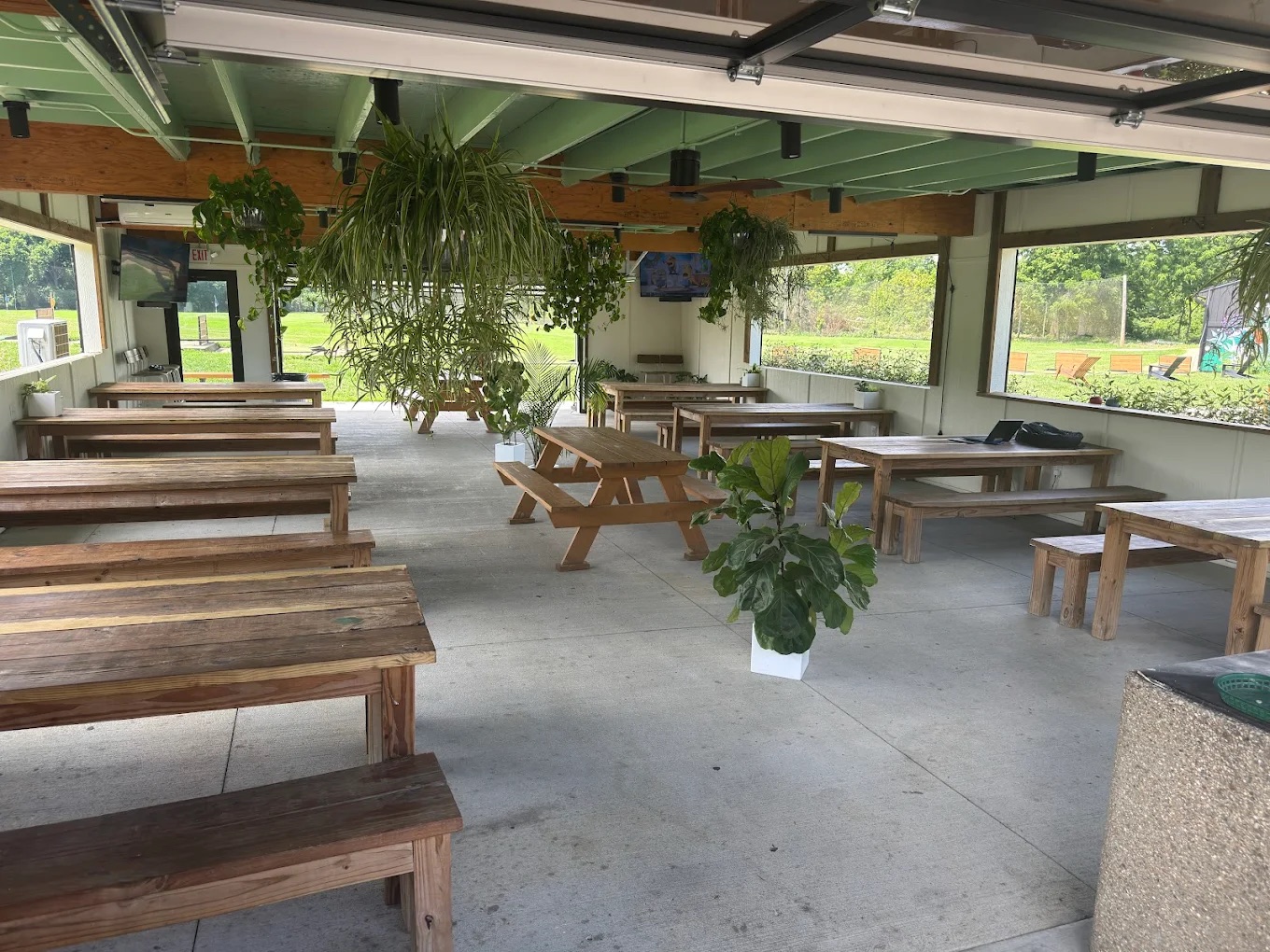 The Acres covered patio — picnic tables, hanging plants, and garage doors open to the range