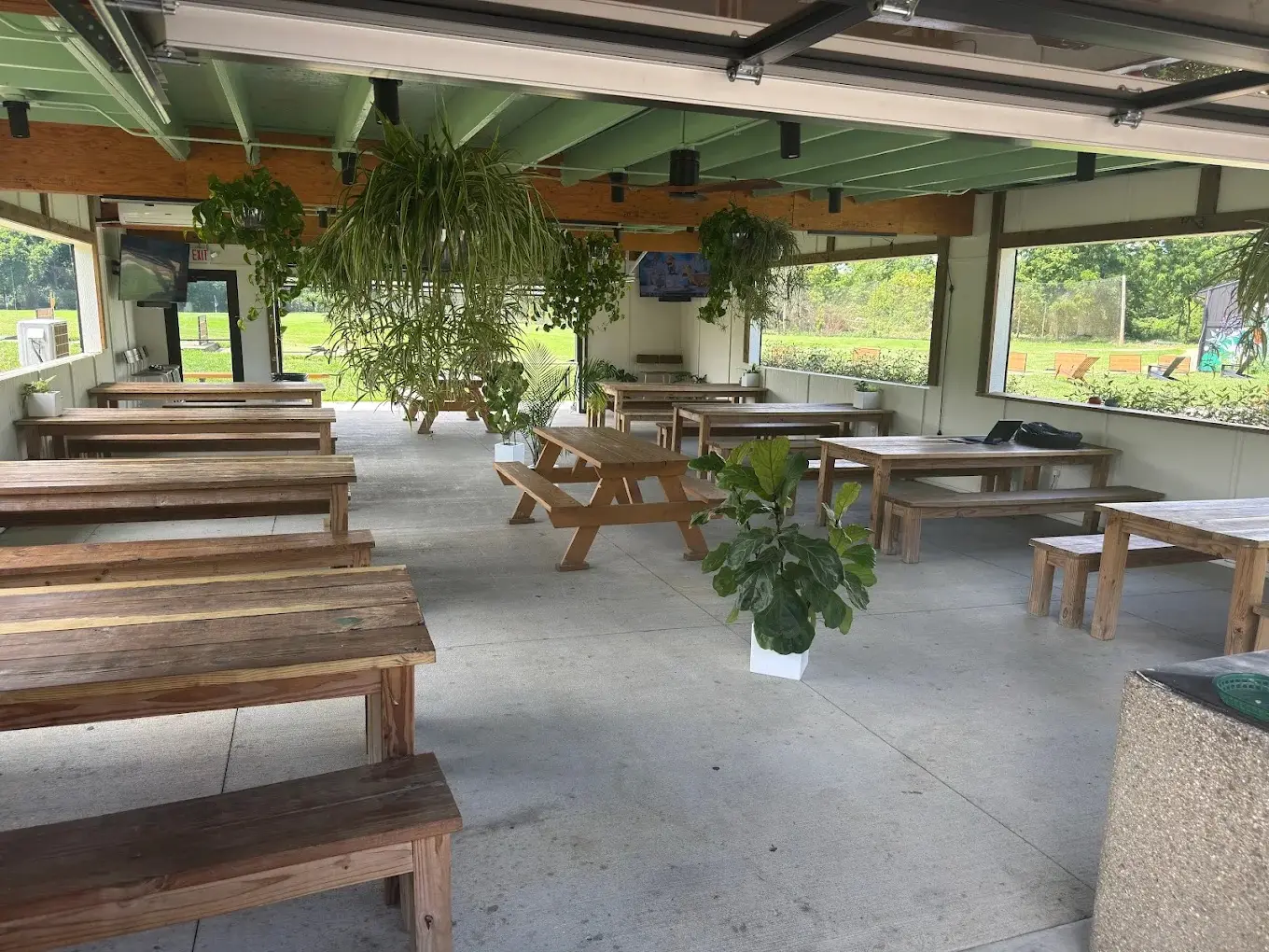 The Acres covered patio — picnic tables, hanging plants, and garage doors open to the range